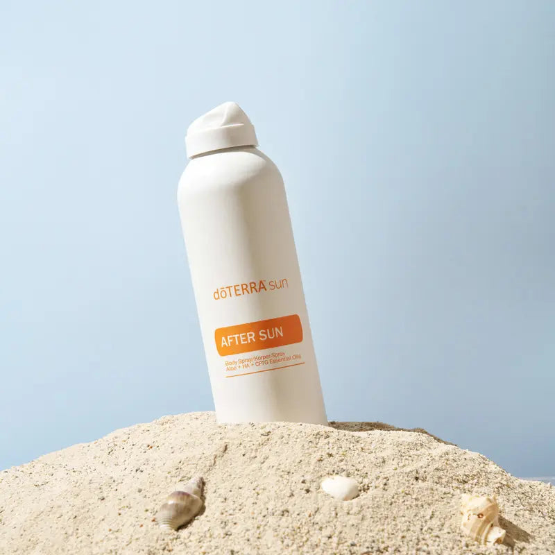 Spray After Sun doTERRA 170g — frasco na areia com conchas, fundo azul pastel, aromaterapia, cuidado da pele