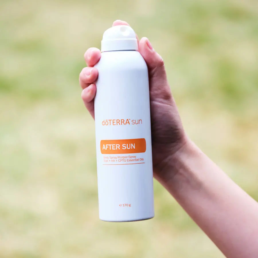 Spray After Sun doTERRA 170g — mão a segurar frasco com fundo de erva verde, hidratação natural