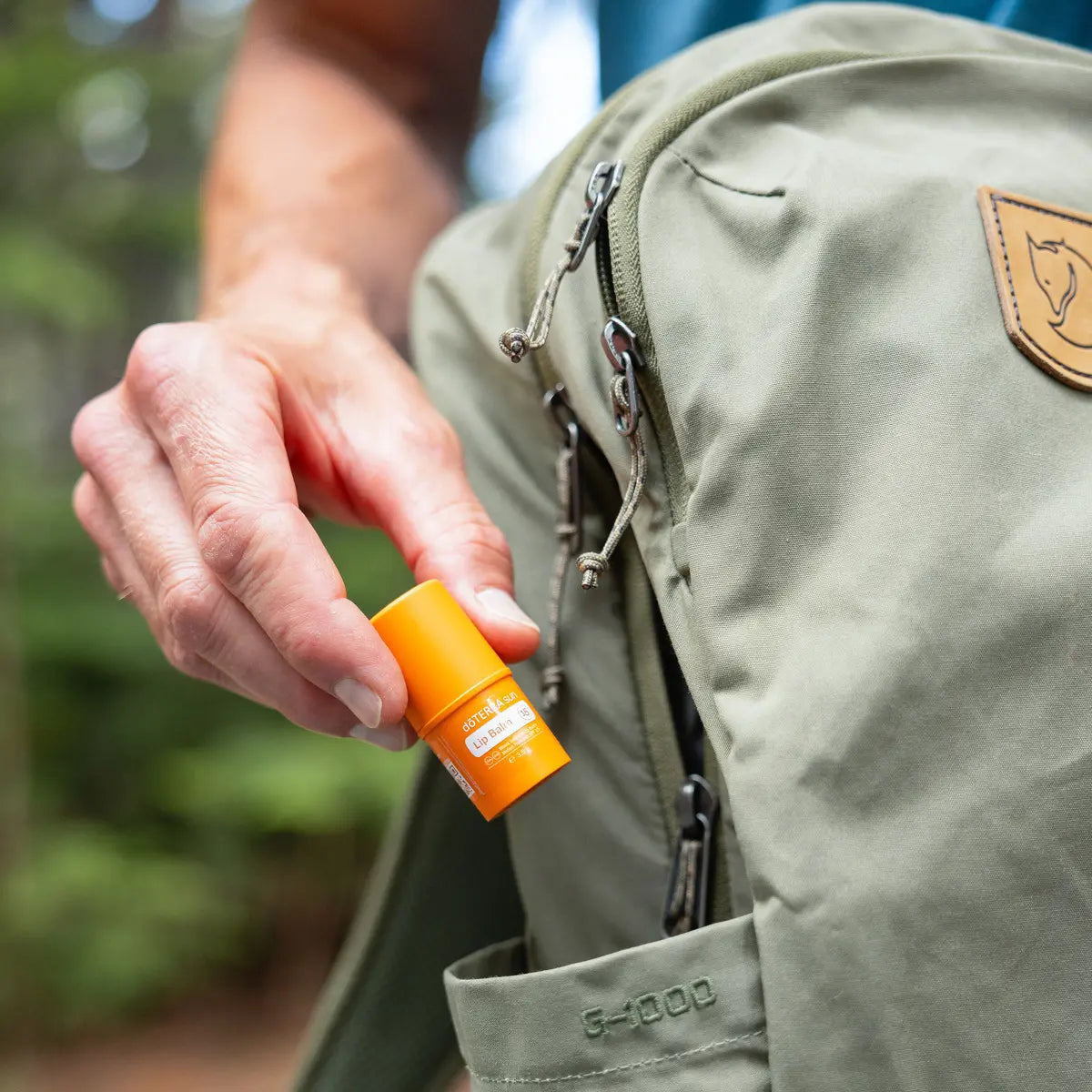 Bálsamo Labial Sun doTERRA SPF15 — mão a retirar da mochila em contexto de trekking na floresta, proteção solar labial