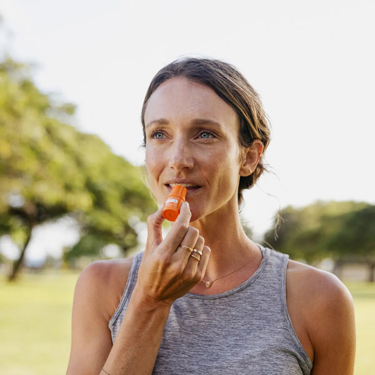 Bálsamo Labial Sun doTERRA SPF15 — mulher a aplicar nos lábios em parque exterior, hidratação e proteção solar CPTG