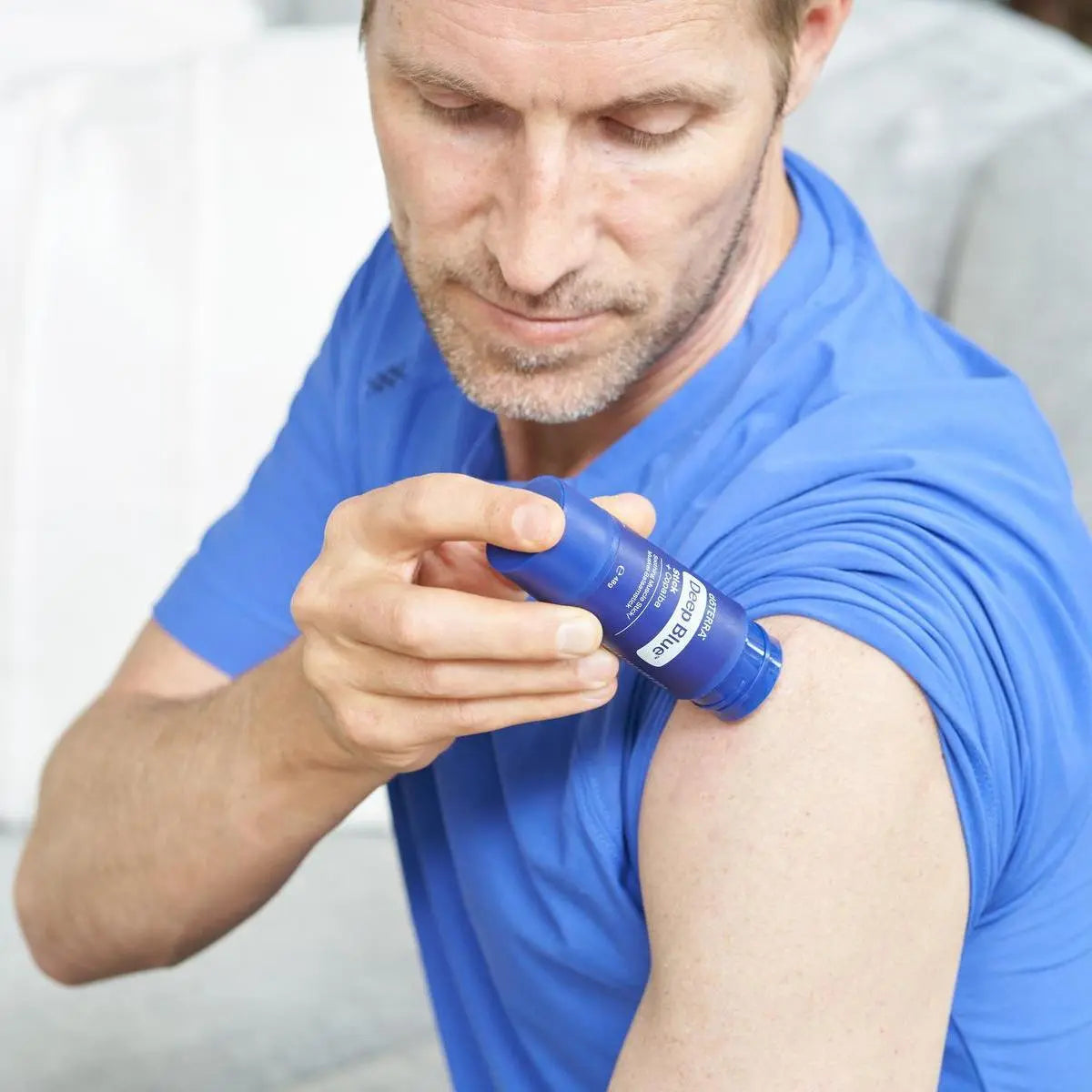 Barra Deep Blue® doTERRA — homem de polo azul a aplicar no ombro em primeiro plano, alívio muscular e articular