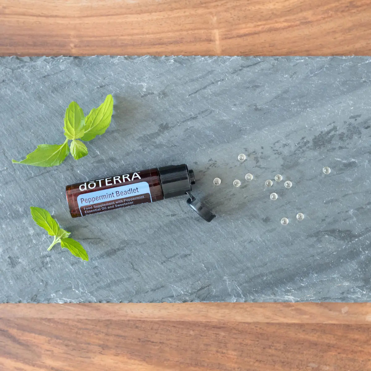 Bolinhas Hortelã-Pimenta Beadlets doTERRA — sobre ardósia cinzenta com folhas de hortelã, vista zenital, óleo essencial CPTG