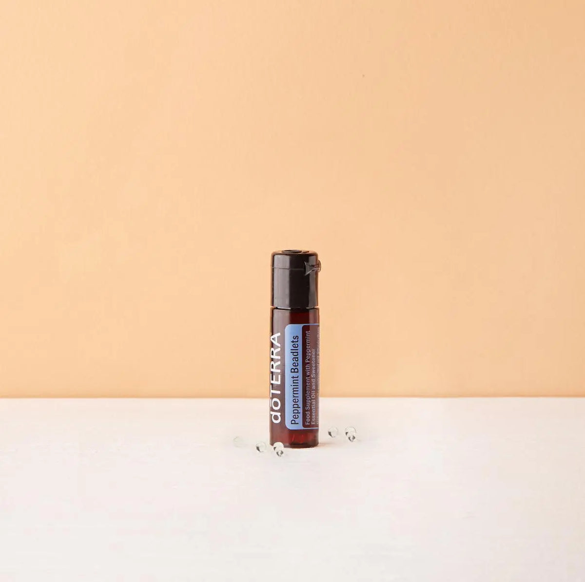 Bolinhas Hortelã-Pimenta Beadlets doTERRA — sobre superfície branca com fundo pêssego, pérolas espalhadas