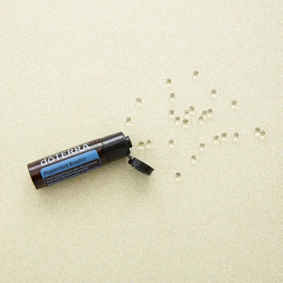 Bolinhas Hortelã-Pimenta Beadlets doTERRA — sobre superfície dourada com pérolas espalhadas, vista zenital, aromaterapia
