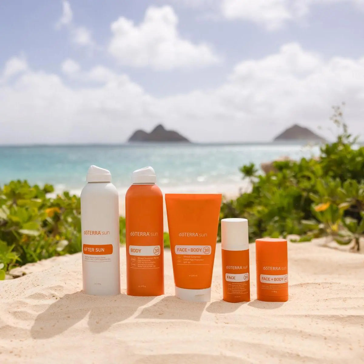 Protetor Solar Mineral doTERRA — gama completa em praia de areia com mar e ilha tropical ao fundo