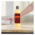 On Guard Concentrado doTERRA 355ml — primeiro plano de mão limpando superfície de madeira, produto natural