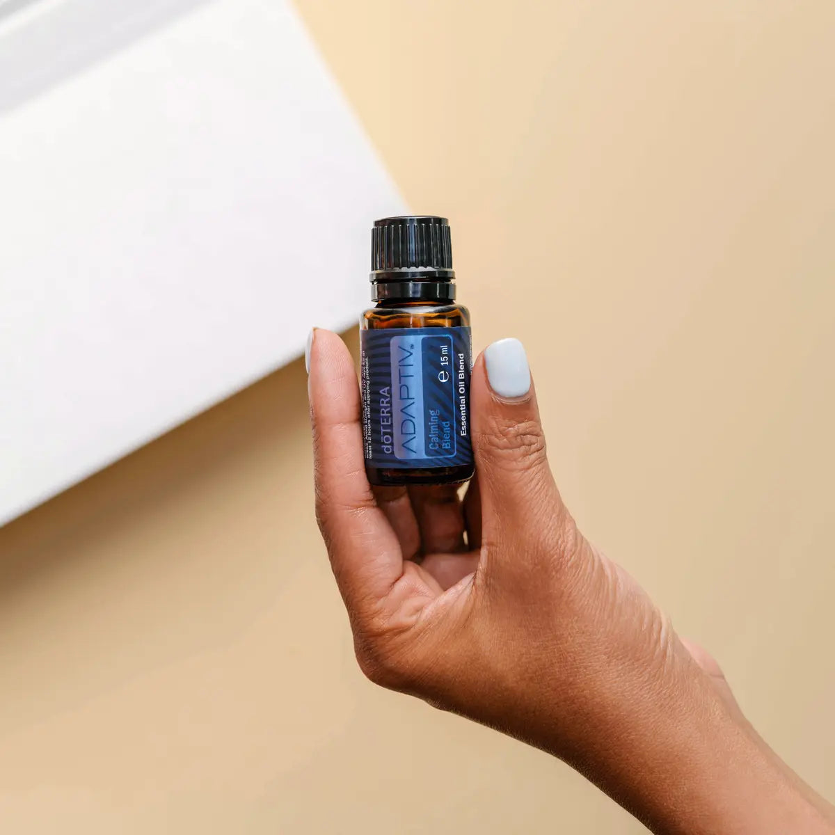 Mistura Adaptiv doTERRA 15ml — mão de pele escura a segurar frasco em fundo bege, aromaterapia calmante