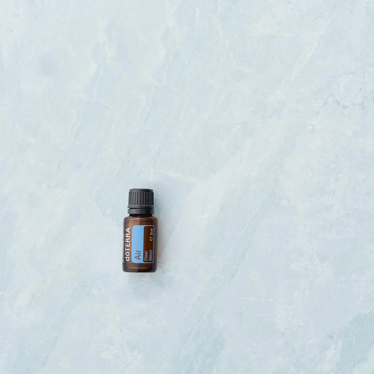 Mistura Air doTERRA 15ml — frasco solo em fundo de mármore azul, vista zenital minimalista, óleo essencial respiratório
