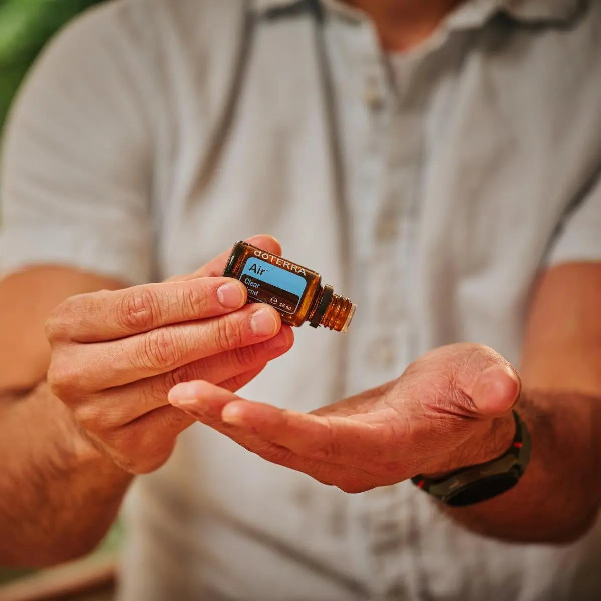 Mistura Air doTERRA 15ml — homem de camisa branca a abrir frasco no exterior com bokeh verde, aromaterapia respiratória