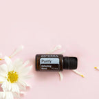Mistura Purify doTERRA 15ml — frasco deitado com pétalas de margarida branca, fundo rosa, vista zenital, aromaterapia