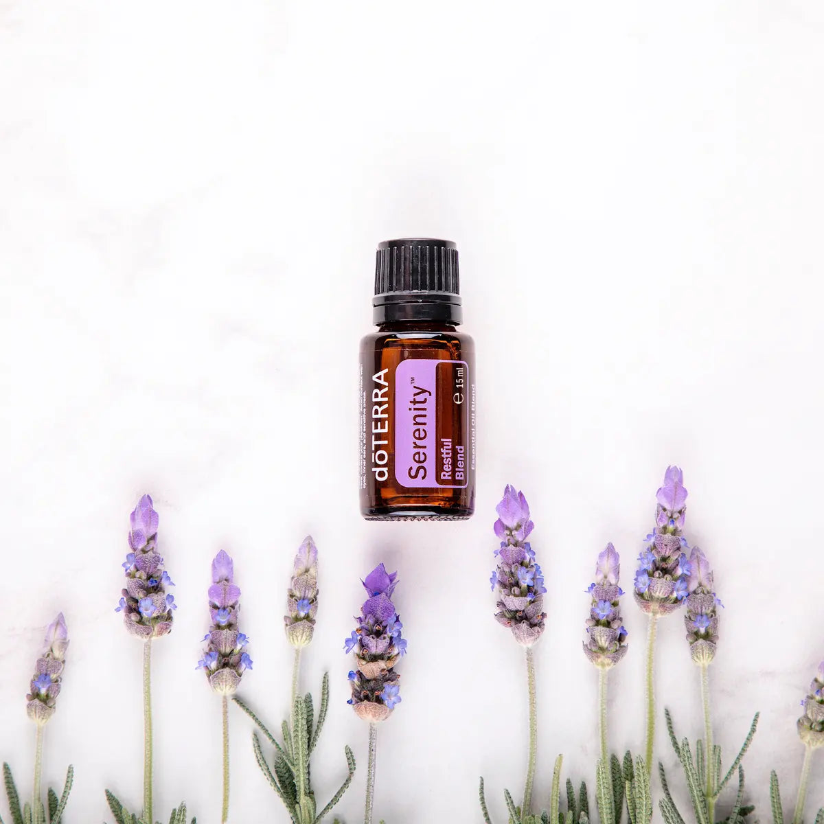 Mistura Serenity doTERRA 15ml — frasco flutuando entre talos de lavanda em mármore branco, vista zenital, aromaterapia