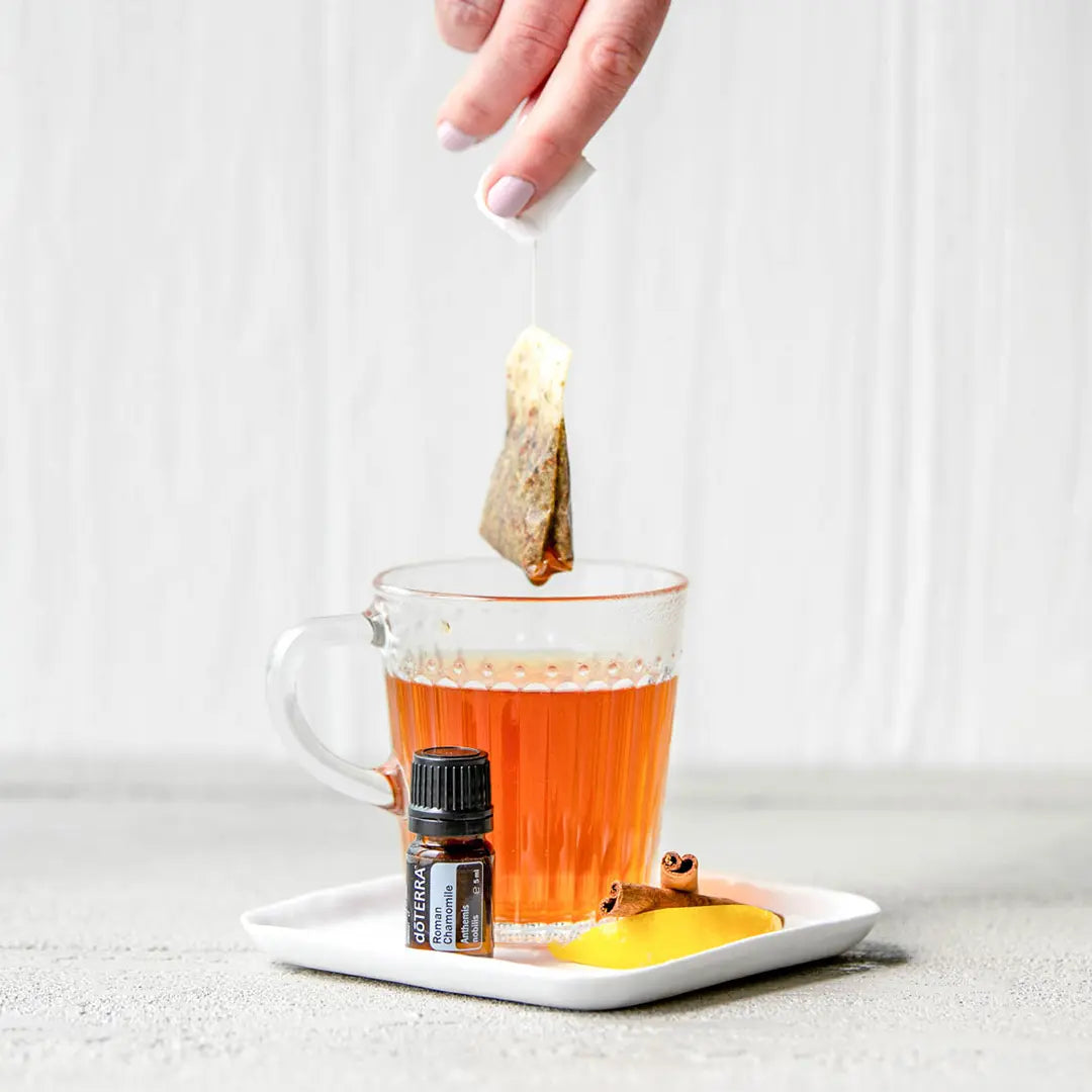 Óleo Essencial Camomila Romana doTERRA 5ml — chávena de vidro com chá, saqueta e canela em pires branco, aromaterapia CPTG