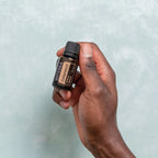 Óleo Essencial Cedro doTERRA 15ml — mão a segurar frasco junto a parede cinzenta, bem-estar natural