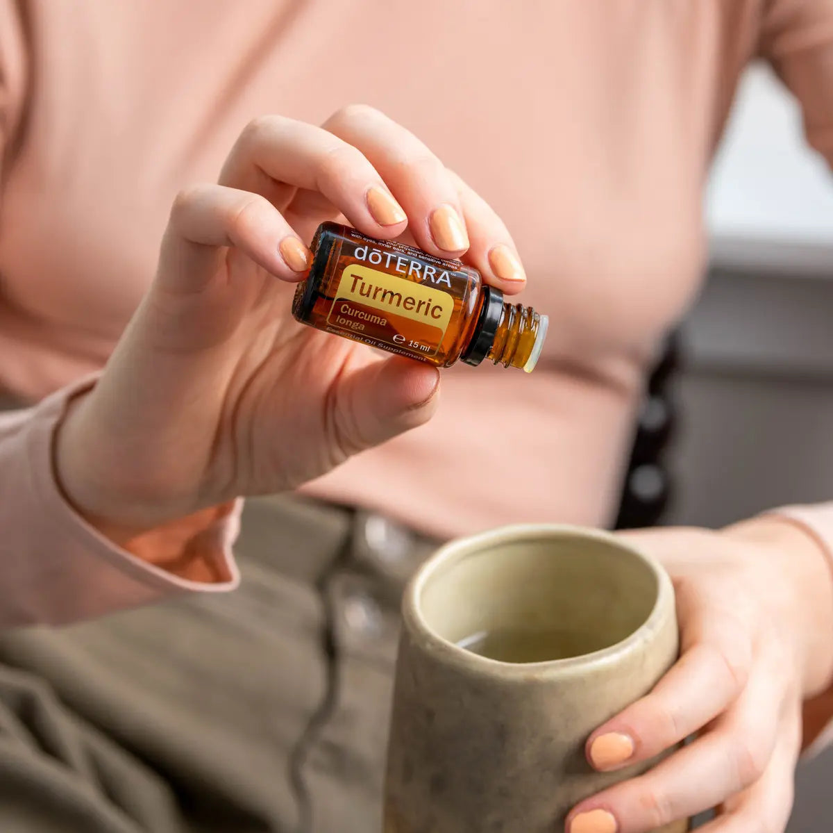 Óleo Essencial Cúrcuma doTERRA 15ml — mãos com frasco e chávena de cerâmica, ritual de bem-estar natural