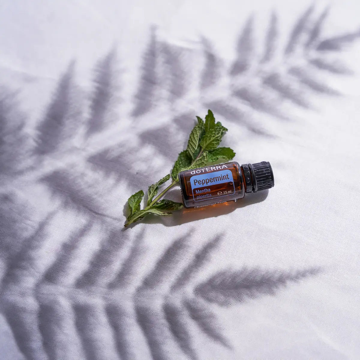 Óleo Essencial Hortelã-Pimenta doTERRA 15ml — raminho de hortelã sobre tecido branco com sombra suave, planta fresca