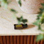 Óleo Essencial Manjerona doTERRA 15ml — frasco sobre bancada de mármore bege com vaso de cerâmica texturizada, aromaterapia, óleo essencial puro CPTG