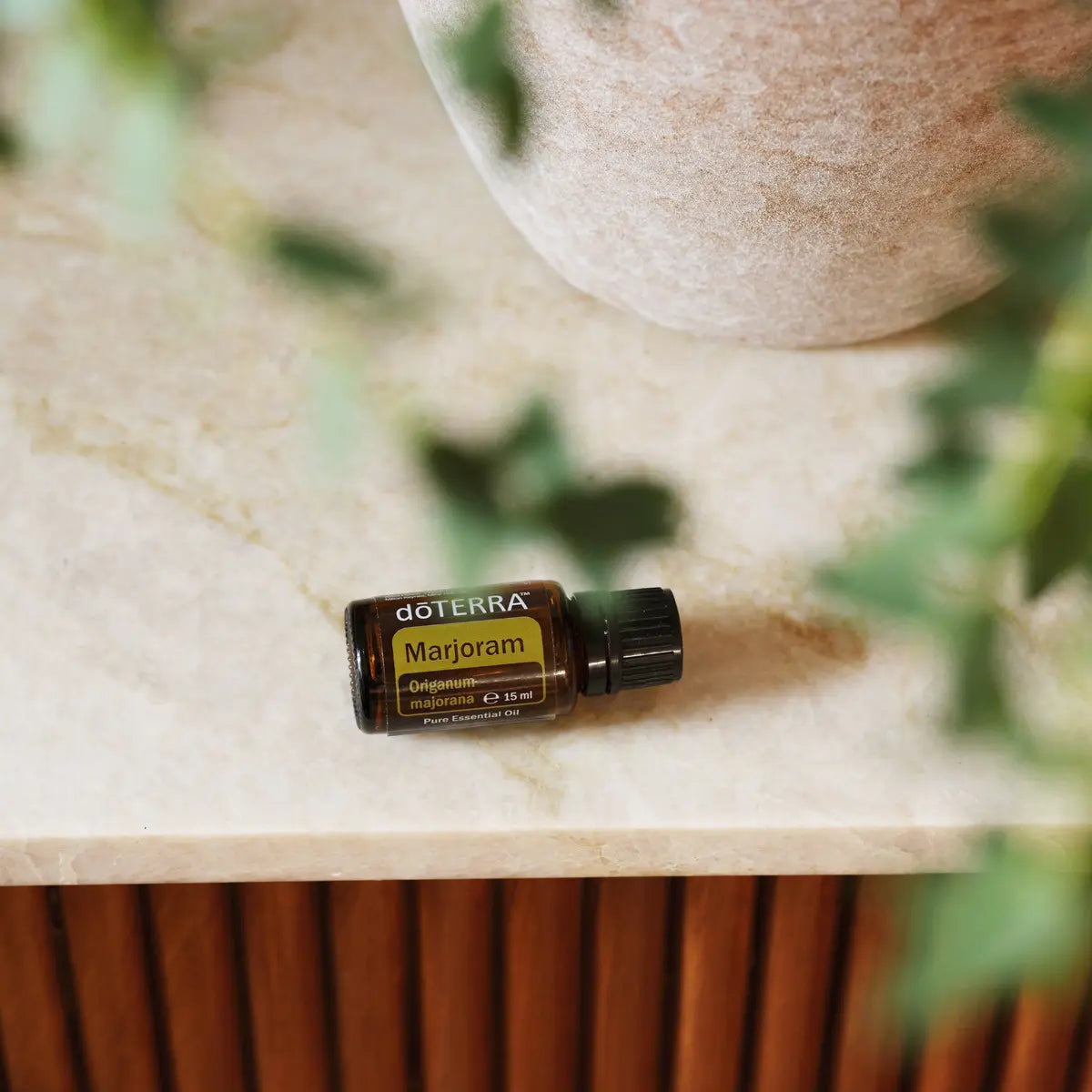 Óleo Essencial Manjerona doTERRA 15ml — frasco sobre bancada de mármore bege com vaso de cerâmica texturizada, aromaterapia, óleo essencial puro CPTG