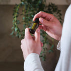 Óleo Essencial Manjerona doTERRA 15ml — mãos com camisola branca seguram frasco junto a planta pendente com folha verde, aromaterapia, óleo essencial puro CPTG