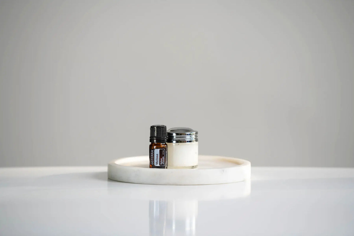 Óleo Essencial Melissa doTERRA 5ml — frasco sobre bandeja de mármore branco com frasco de creme, fundo cinzento, aromaterapia, óleo essencial puro CPTG
