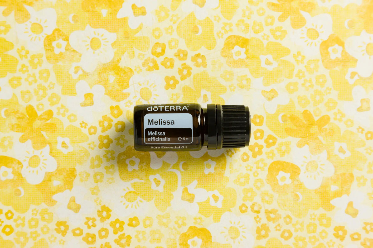 Óleo Essencial Melissa doTERRA 5ml — flat lay com frasco sobre tecido estampado floral amarelo, aromaterapia, óleo essencial puro CPTG