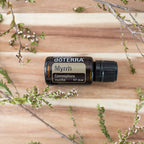 Óleo Essencial Mirra doTERRA 15ml — flat lay sobre tábua de madeira quente com ramos de flores brancas, aromaterapia, óleo essencial puro CPTG