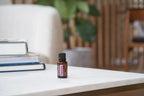 Óleo Essencial Patchouli doTERRA 15ml — frasco sobre mesa de mármore com livros, vaso e estante de lamas de madeira, aromaterapia, óleo essencial puro CPTG