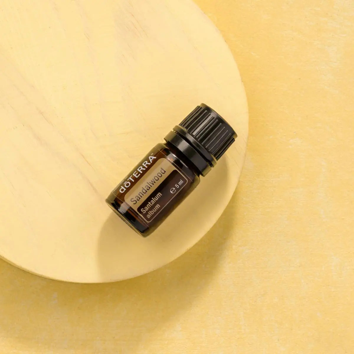 Óleo Essencial Sândalo Indiano doTERRA 5ml — disco de madeira natural com fundo amarelo minimalista, aromaterapia, óleo essencial puro CPTG