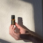 Óleo Essencial Sândalo Indiano doTERRA 5ml — mão a segurar frasco com sombra em parede texturizada à luz solar, aromaterapia, óleo essencial puro CPTG