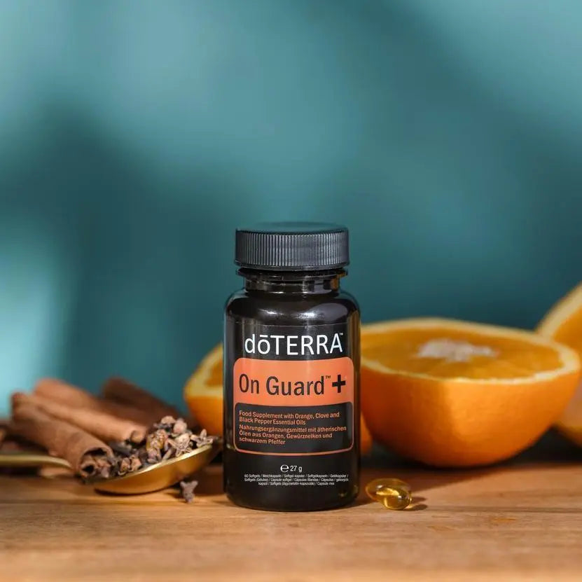 On Guard+ Softgels doTERRA — frasco em tábua de madeira com laranja, canela e cravo, fundo teal, óleo essencial CPTG