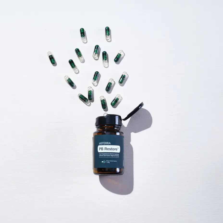 PB Restore doTERRA — frasco aberto com cápsulas em explosão zenital, suplemento microbioma natural CPTG