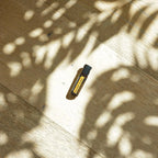 Beadlets MetaPWR doTERRA — frasco no chão de parque, madeira com sombras de árvore, suplemento bem-estar CPTG