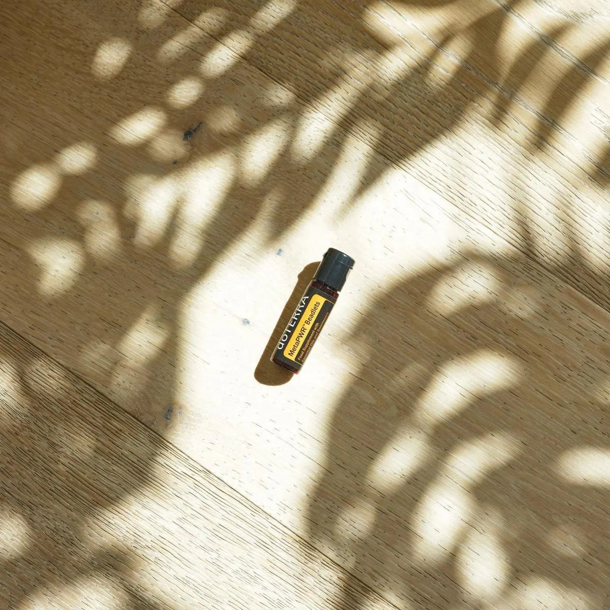 Beadlets MetaPWR doTERRA — frasco no chão de parque, madeira com sombras de árvore, suplemento bem-estar CPTG