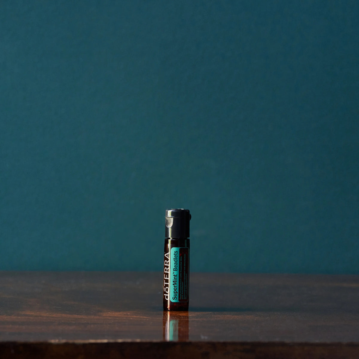 Beadlets Supermint doTERRA — frasco em mesa de madeira escura, fundo verde azulado, menta refrescante puro CPTG