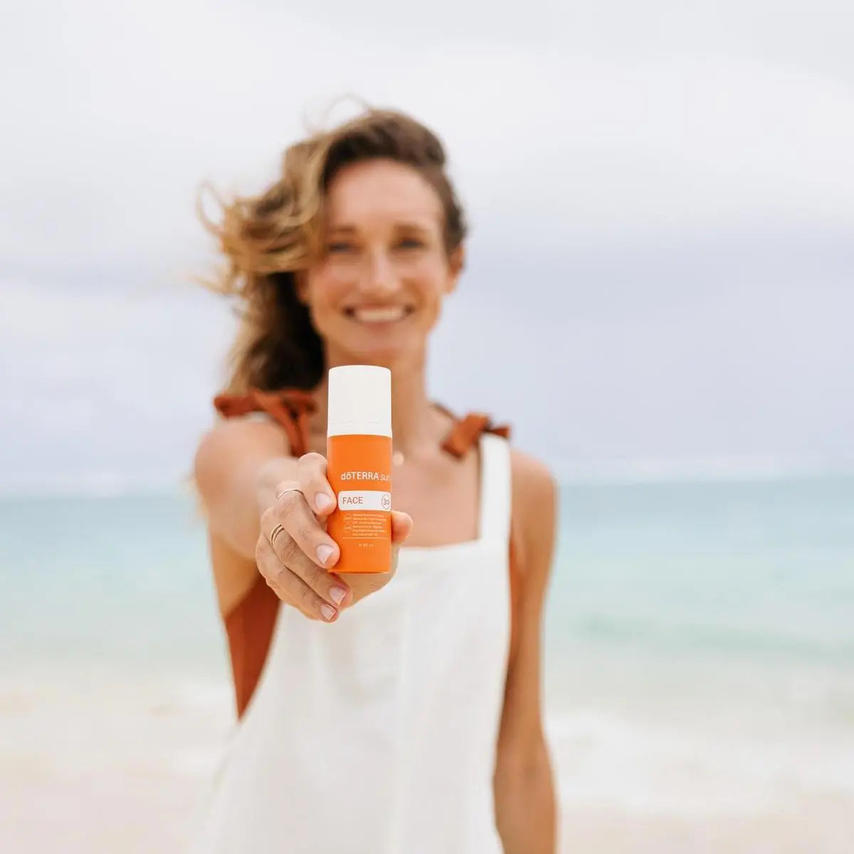 Protetor Solar Mineral Hidratante doTERRA SPF30 — mulher segurando câmara na praia com vento, cuidado solar facial CPTG