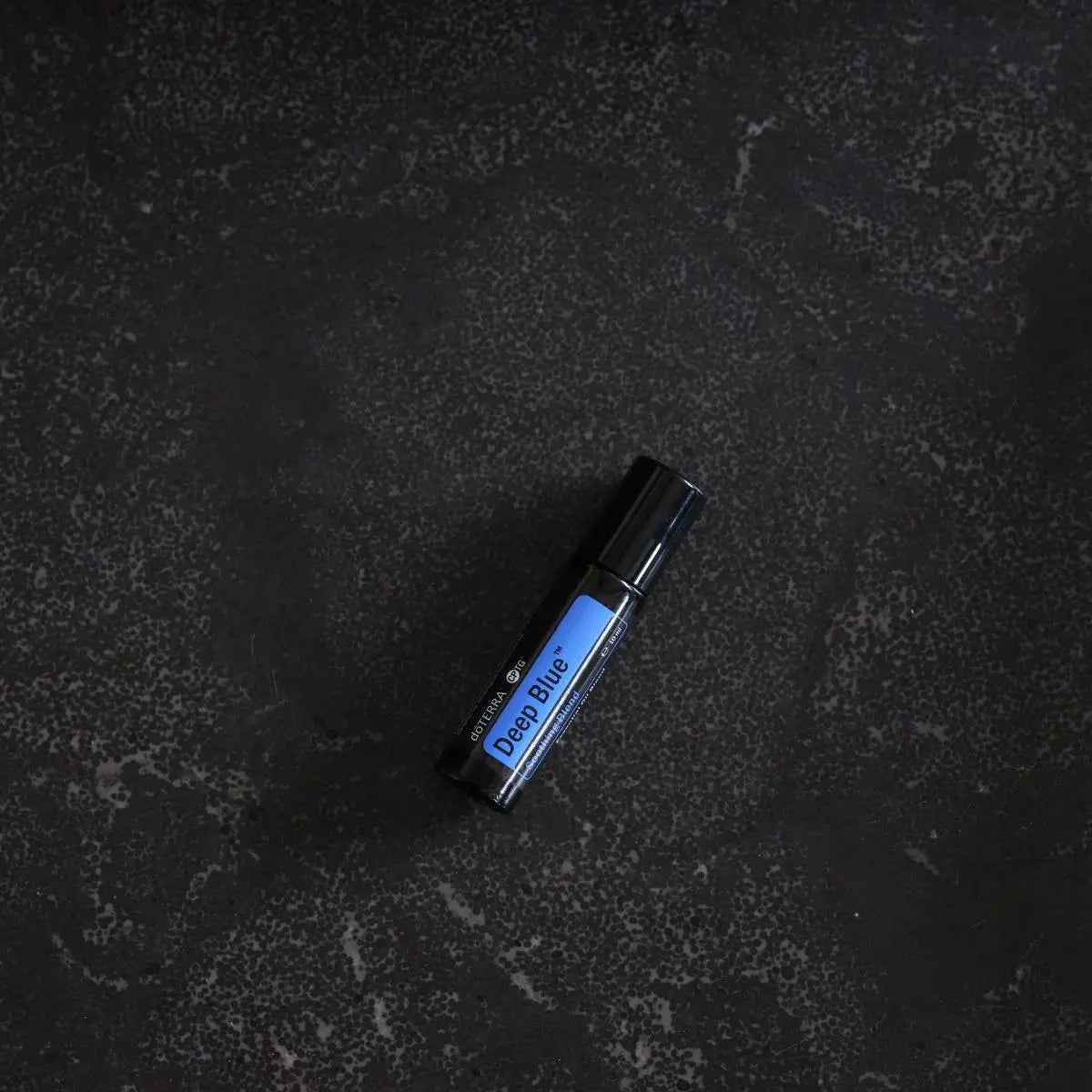 Deep Blue Touch doTERRA Roll-on 10ml — deitado em granito preto texturizado cenital, óleo musão puro CPTG