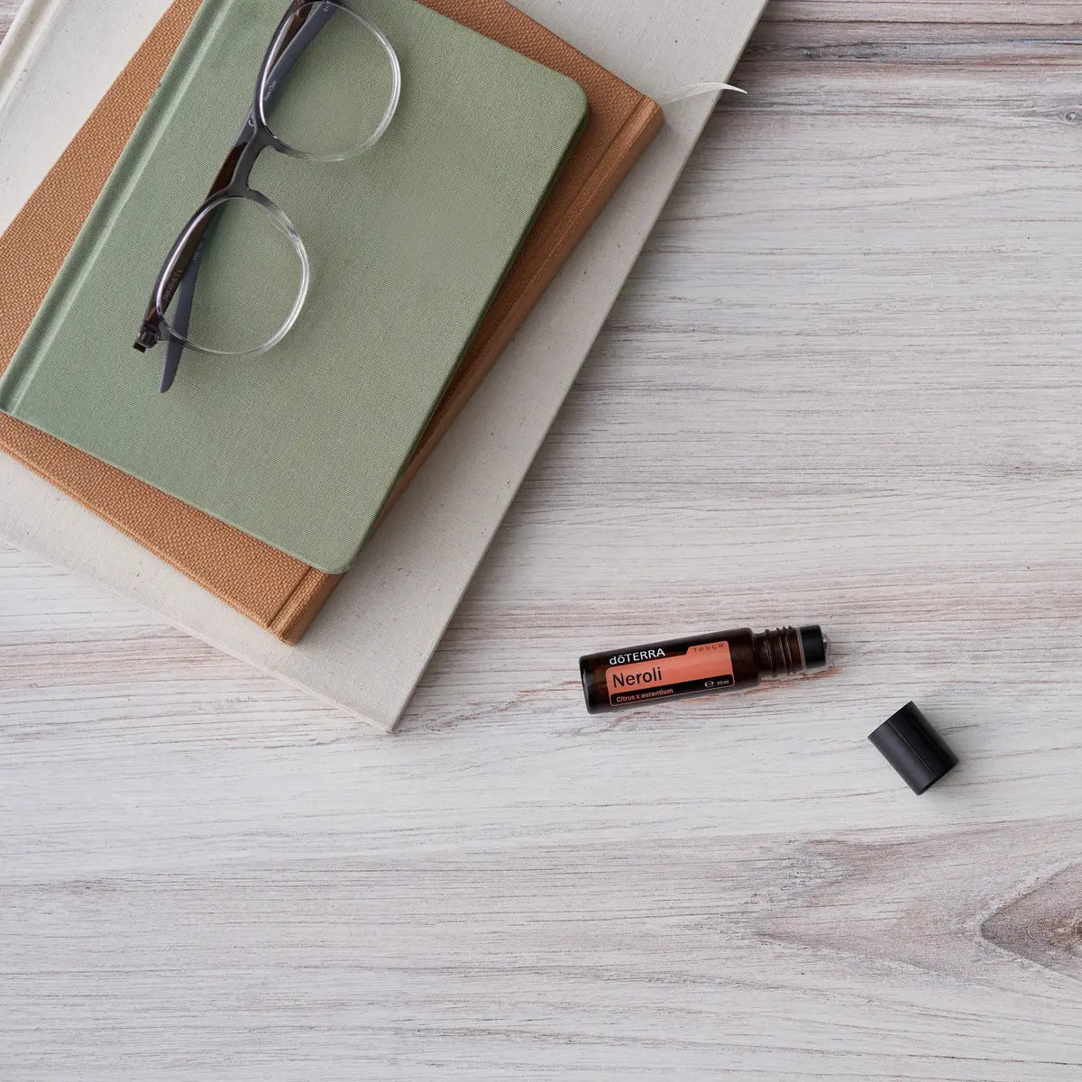 Roll-On Neroli Touch doTERRA 10ml — deitado com livros e óculos em madeira branca, óleo essencial neroli CPTG