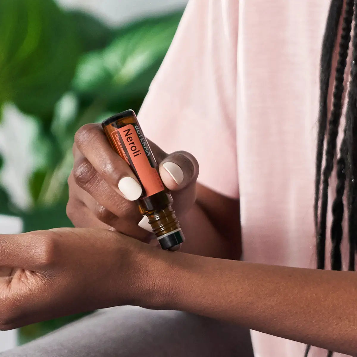 Roll-On Neroli Touch doTERRA 10ml — mulher de pele escura a aplicar no pulso com planta ao fundo, óleo essencial puro