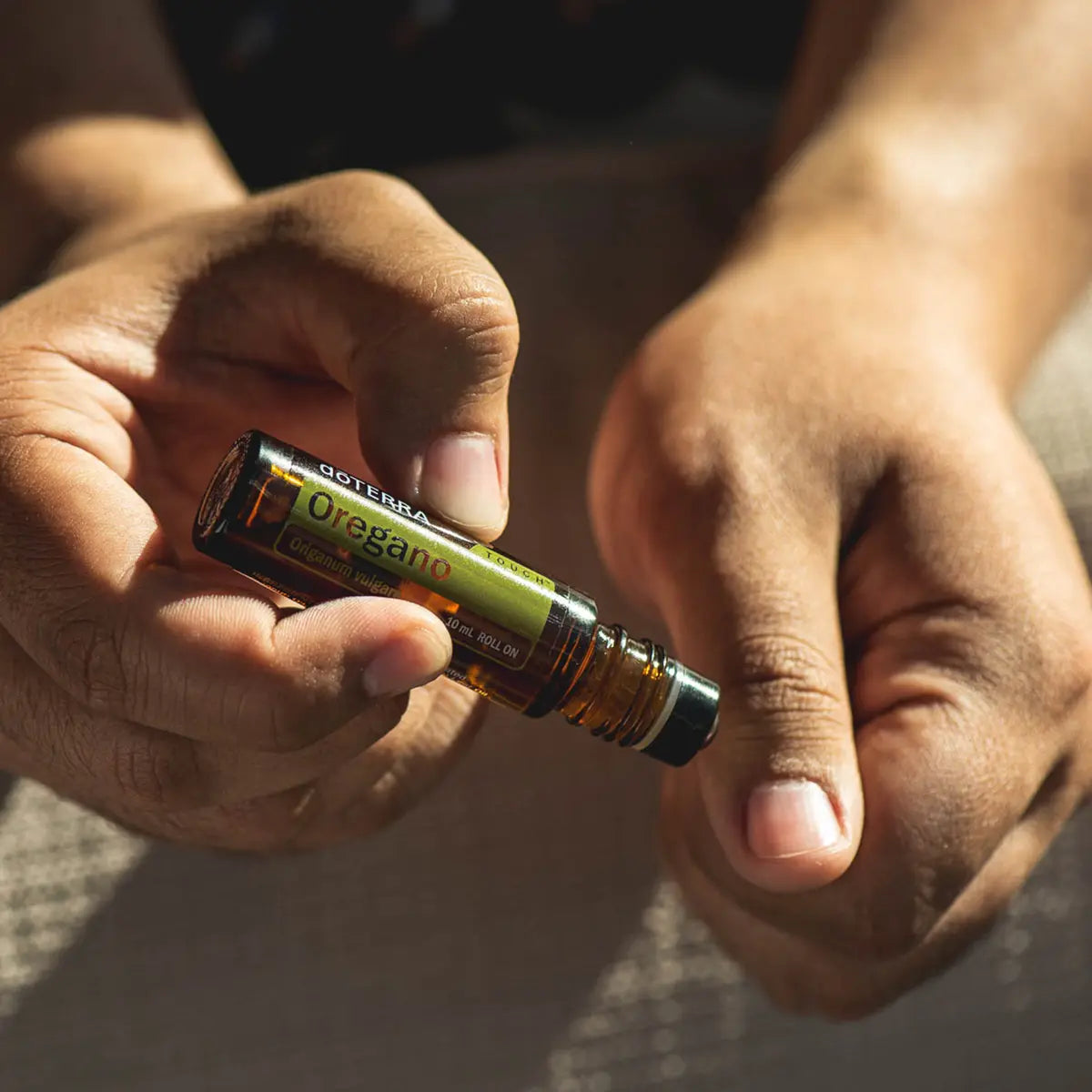 Roll-On Oregão Touch doTERRA 10ml — mãos a aplicar na pele com luz solar quente, aromaterapia oregão doTERRA