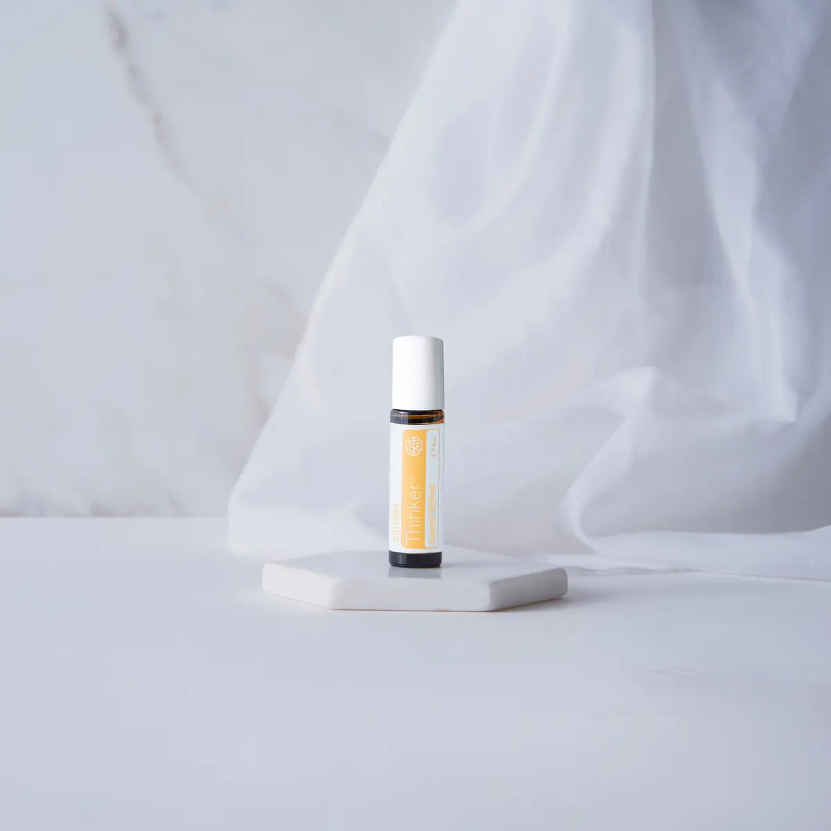 Thinker doTERRA Roll-On 10ml — pedestal branco com tecido drapeado em mármore, óleo essencial foco CPTG