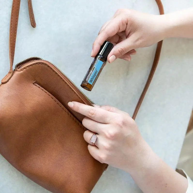 Whisper Touch doTERRA Roll-On 10ml — mãos a tirar da mala em pele castanha, perfume natural feminino CPTG