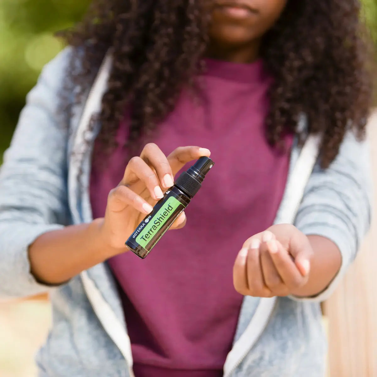 TerraShield doTERRA Spray 30ml — menina de cabelo encaracolado a aplicar no pulso, exterior jardim, aromaterapia