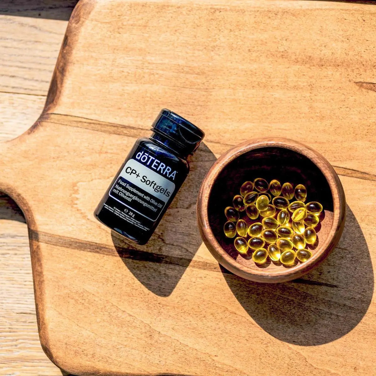 Cápsulas Moles CP+ doTERRA — frasco com tigela madeira e softgels em tábua, vista cenital, suplemento proteção celular