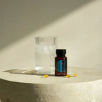 DDR Prime Softgels doTERRA — frasco sobre pedestal de pedra com vaso de água e luz natural, suplemento renovação celular