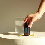 DDR Prime Softgels doTERRA — mão a segurar frasco junto a vaso de água e pedra, suplemento renovação celular