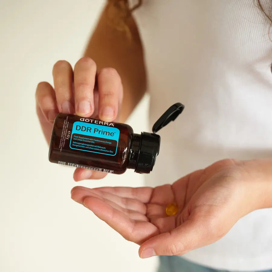 DDR Prime Softgels doTERRA — mãos com frasco aberto e softgel na palma, suplemento renovação celular, bem-estar