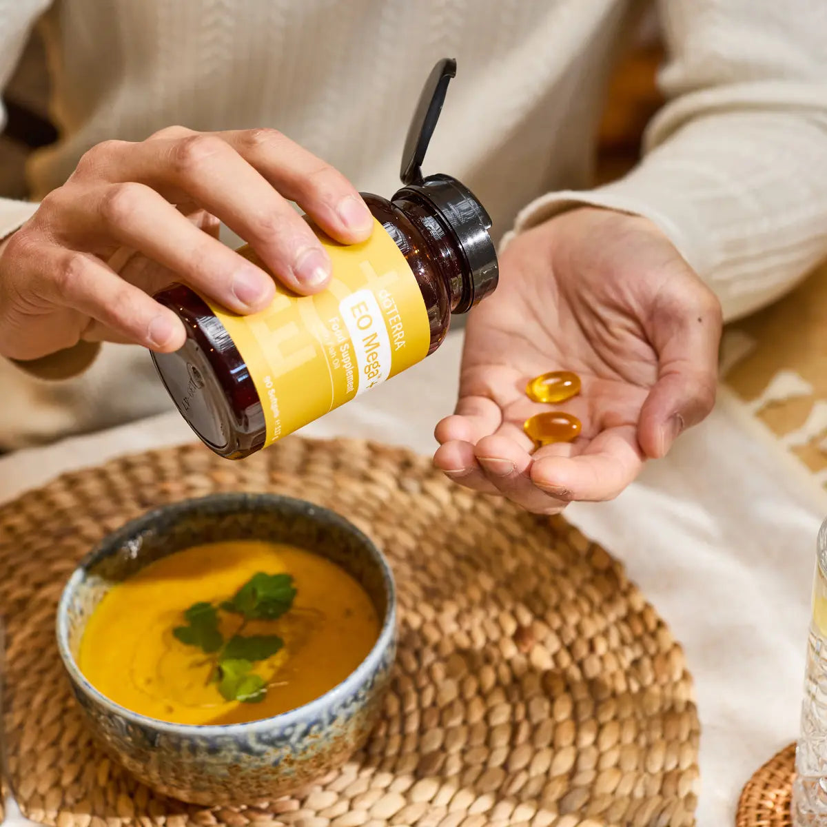 Cápsulas EO Mega+ doTERRA — frasco, mãos e softgels em tigela de sopa, suplemento ómega essencial, bem-estar