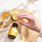 Cápsulas EO Mega+ doTERRA — mão com softgel, limão e vaso de água em bandeja de vime, suplemento ómega essencial
