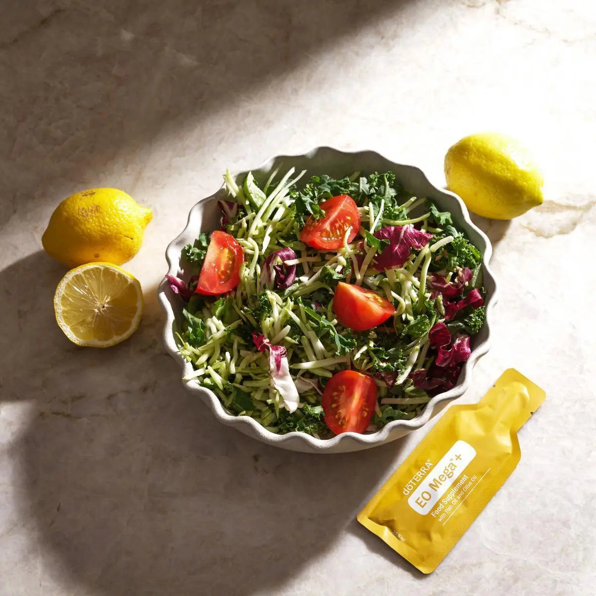 EO Mega+ doTERRA — saqueta com salada verde, tomate e limão sobre mármore, vista cenital, suplemento ómega essencial