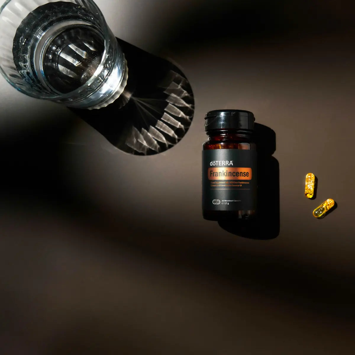 Cápsulas Microesferas Incenso doTERRA — frasco junto a vaso de cristal, fundo escuro, vista aérea, suplemento puro CPTG