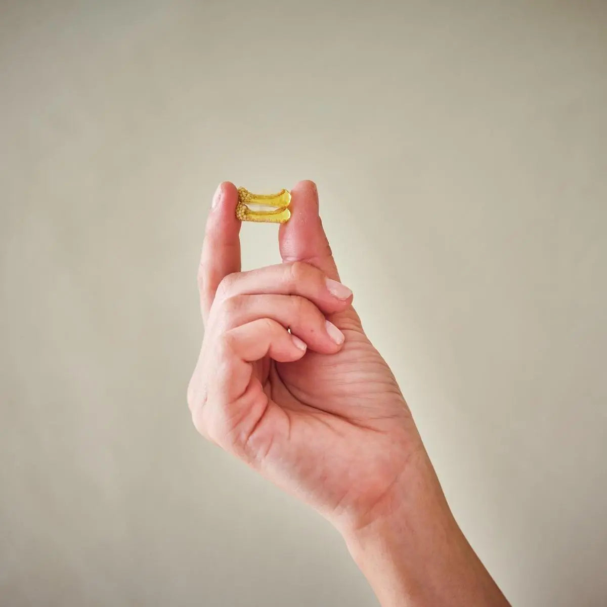 Cápsulas Microesferas Incenso doTERRA — mão a segurar duas cápsulas douradas sobre fundo bege, suplemento natural certificado CPTG